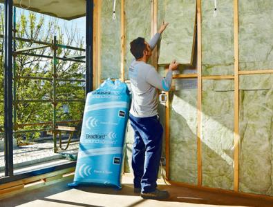Worker fitting glasswool insulation batts into a timber-framed wall beside a window