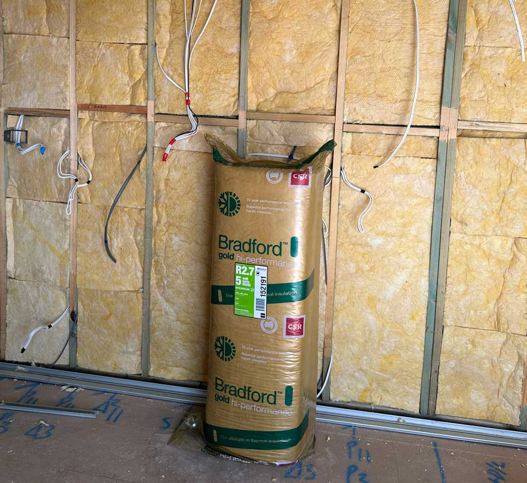 Roll of rockwool insulation standing against a timber-framed wall lined with insulation batts
