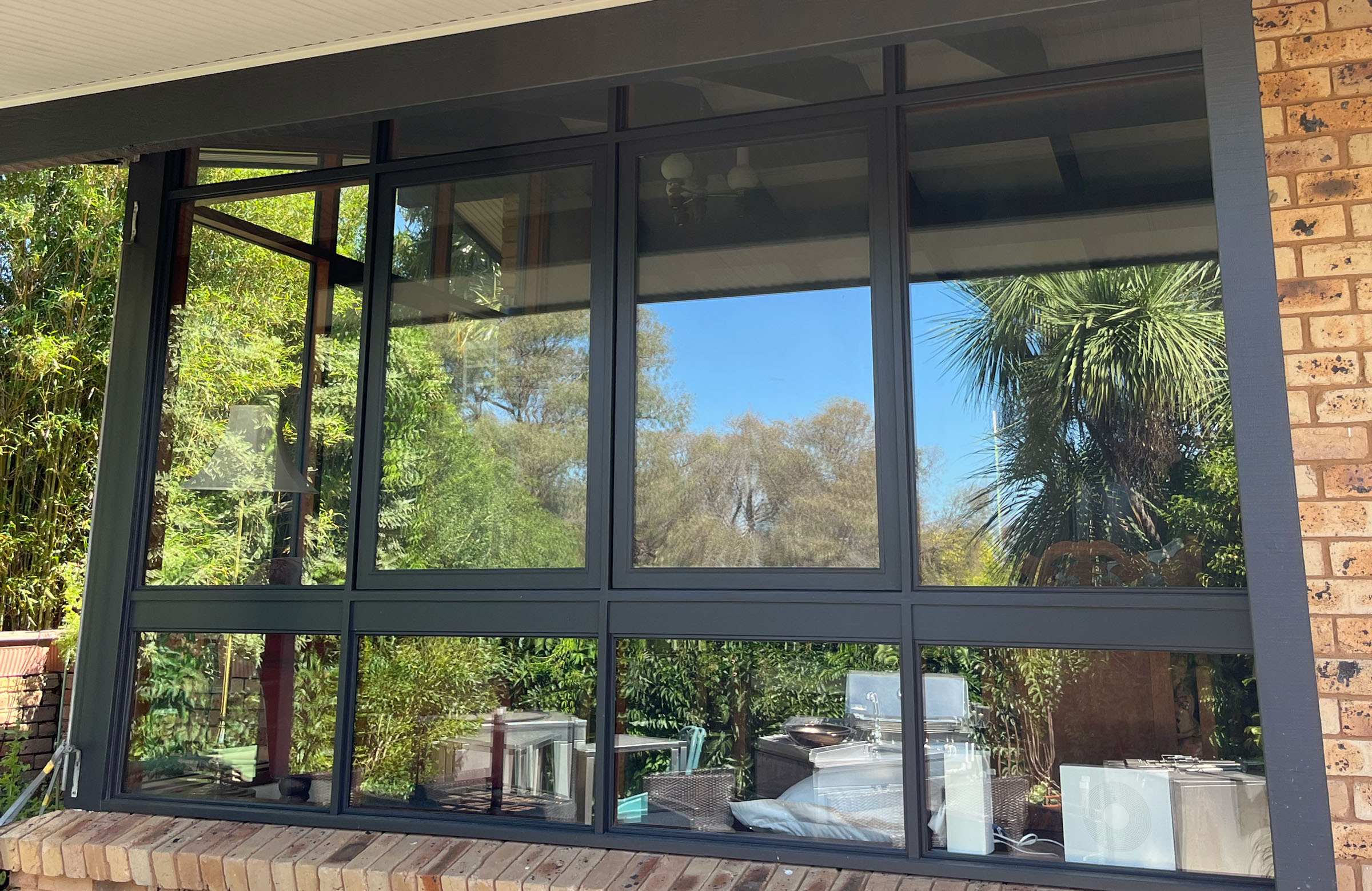 Large dark-framed retrofitted double glazed windows on a brick home, reflecting the front garden