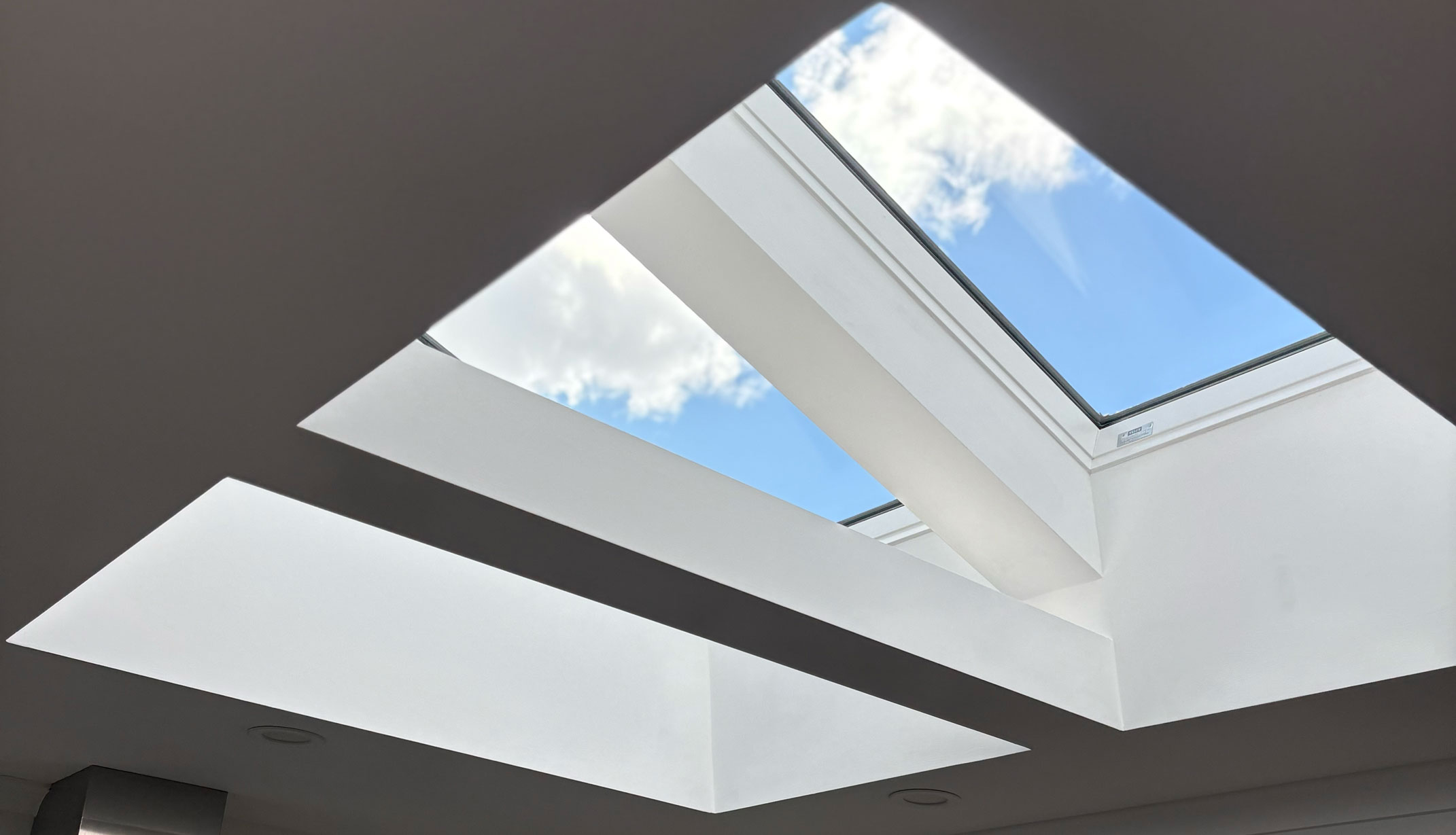 Two VELUX skylights side by side in a white raked ceiling, showing blue sky