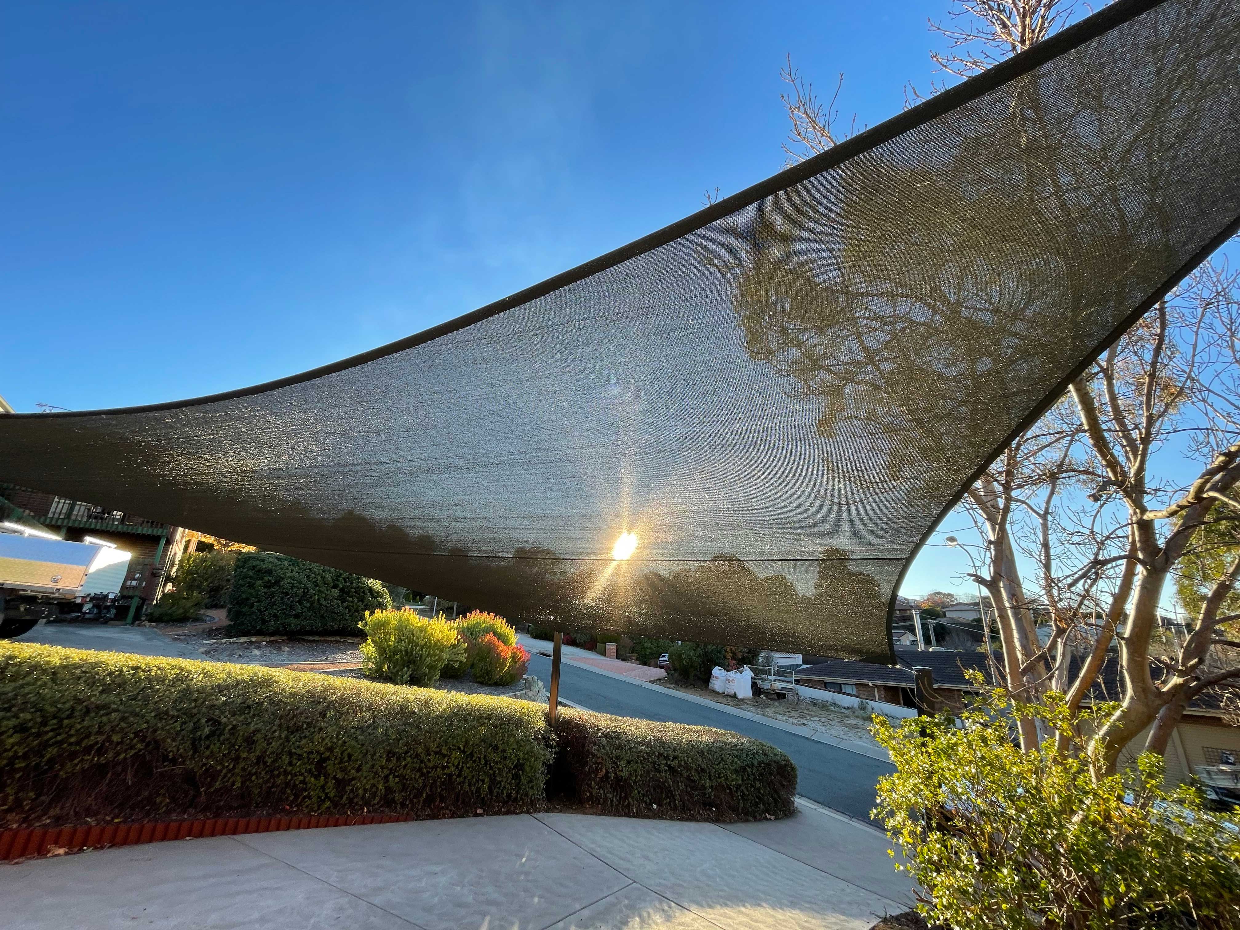 Curved shade sail over a driveway and garden with the late afternoon sun behind it