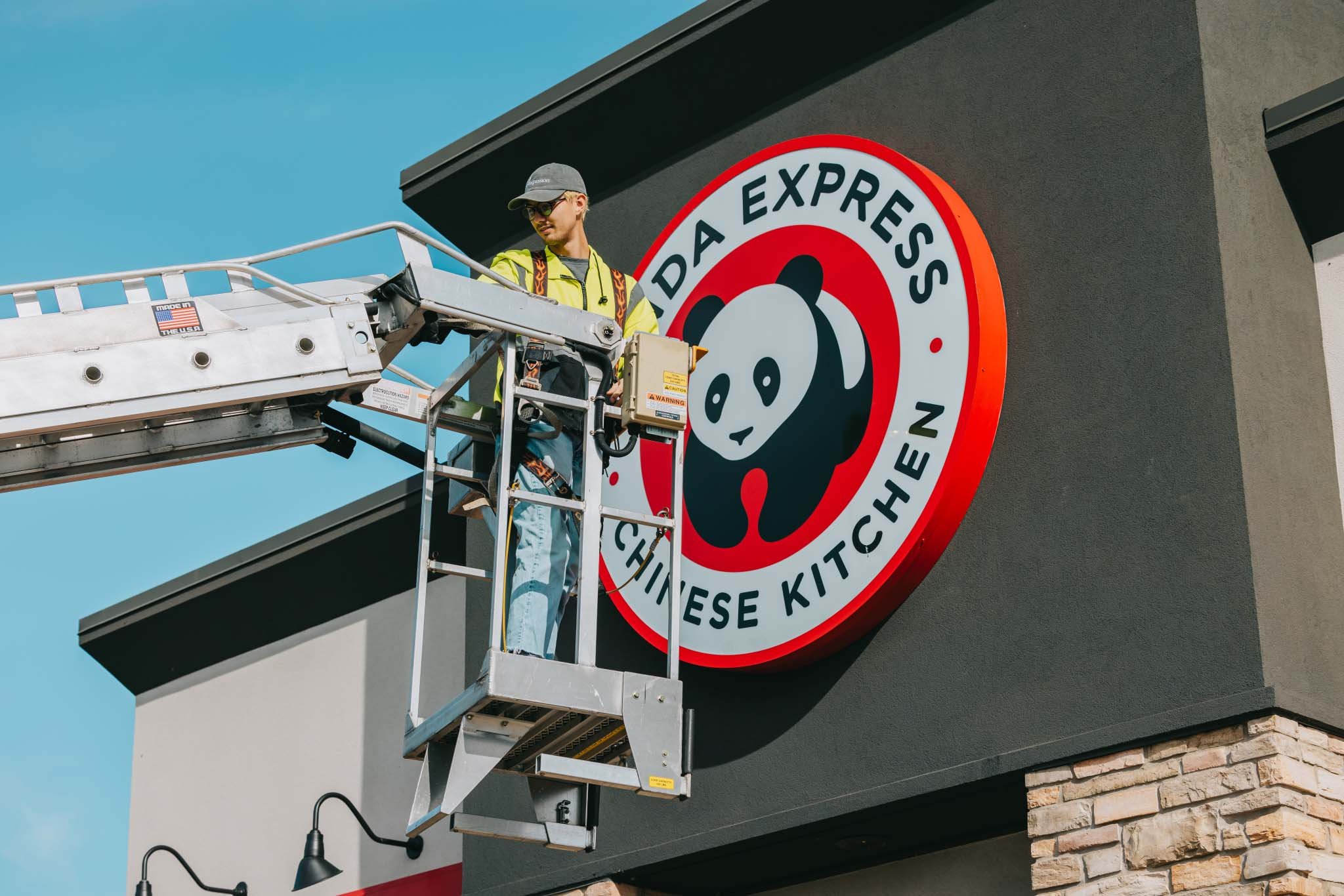 Rick Signs bucket truck repairing the Panda Express round logo storefront sign with autumn trees in the background — Chicago