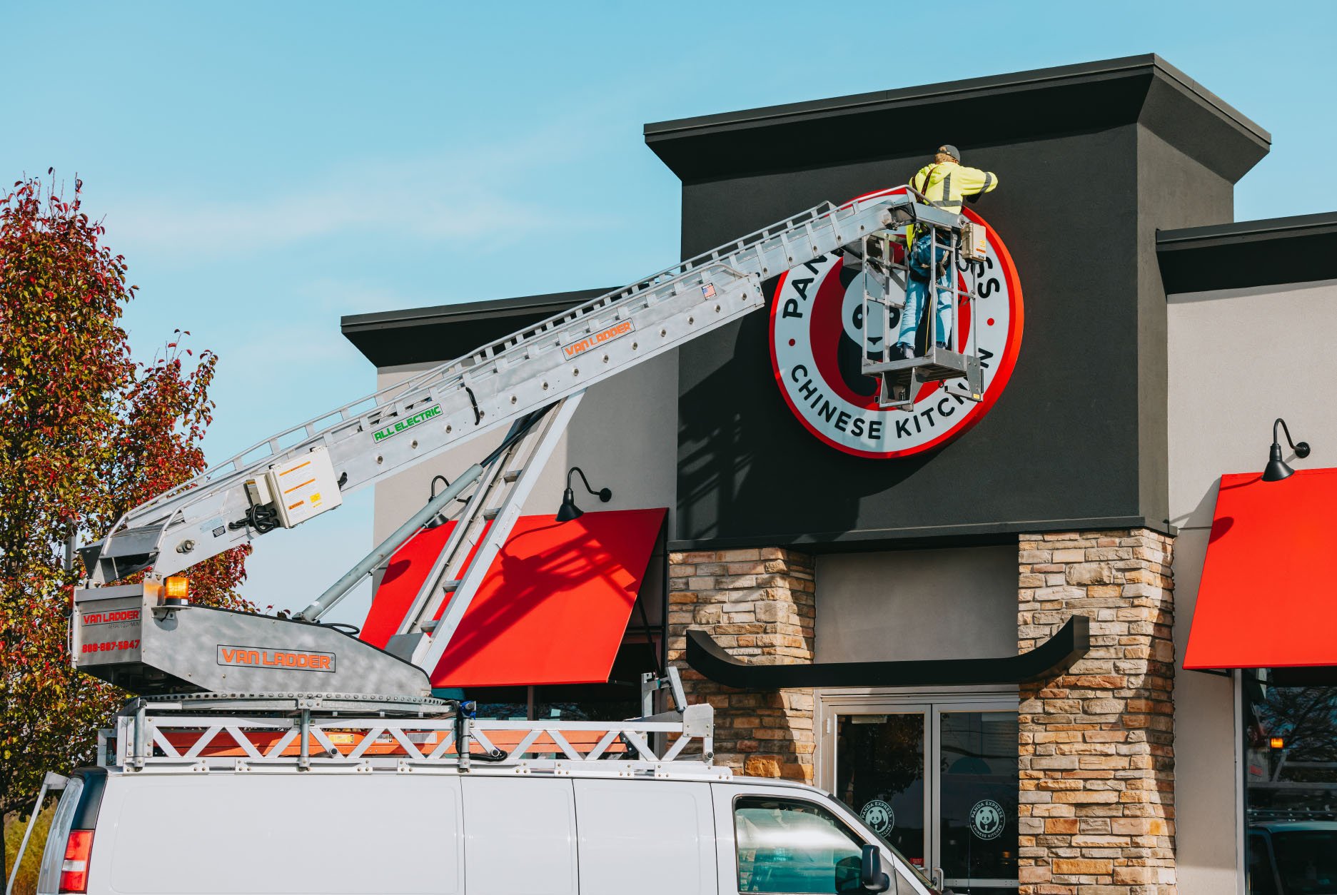 Rick Signs bucket truck servicing the round Panda Express logo storefront sign during autumn in Chicago