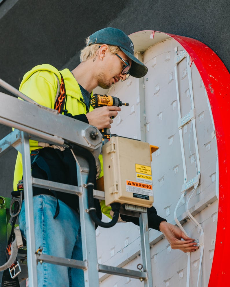 Rick Signs technician working from the bucket truck on the curved red edge of a channel letter sign electrical assembly in Chicago