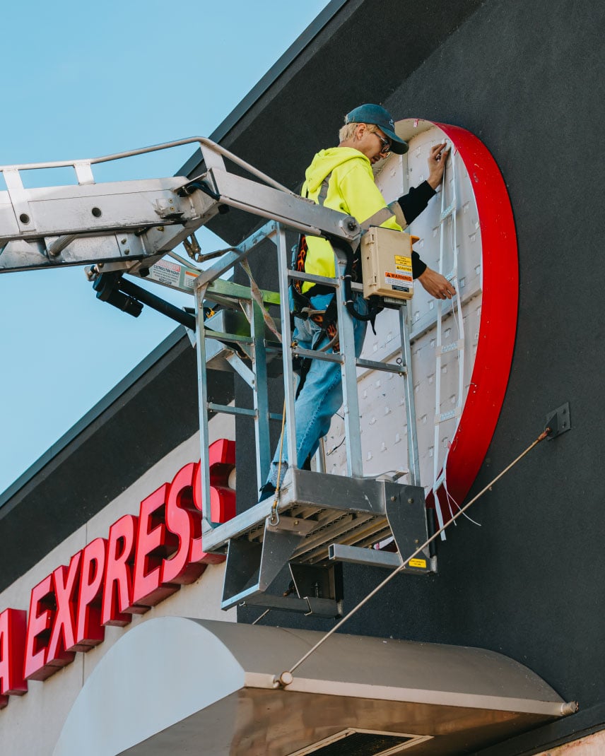 Tymothy Mough working from the bucket truck on a red curved channel letter sign installing LED modules — Rick Signs Chicago
