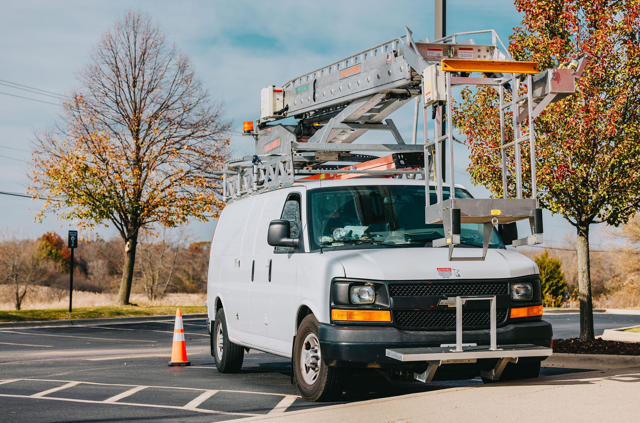 Rick Signs service van and bucket truck arriving at a tall commercial pole sign during autumn in Chicago