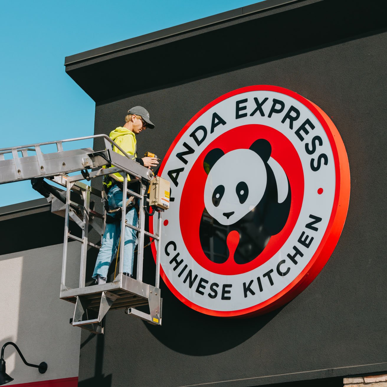 Low-angle view of the Panda Express round logo storefront sign during a Rick Signs service call in Chicago