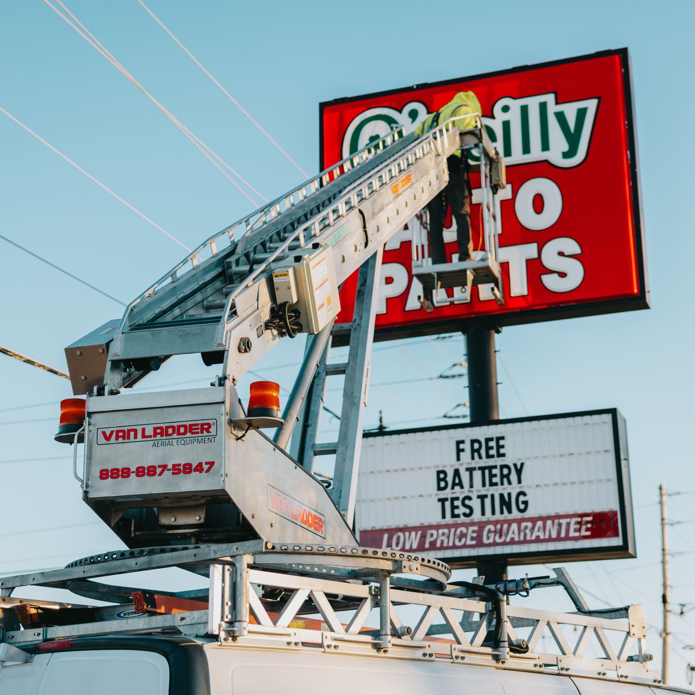 Rick Signs bucket truck servicing the tall O’Reilly Auto Parts pole sign with FREE BATTERY TESTING signage in Chicago