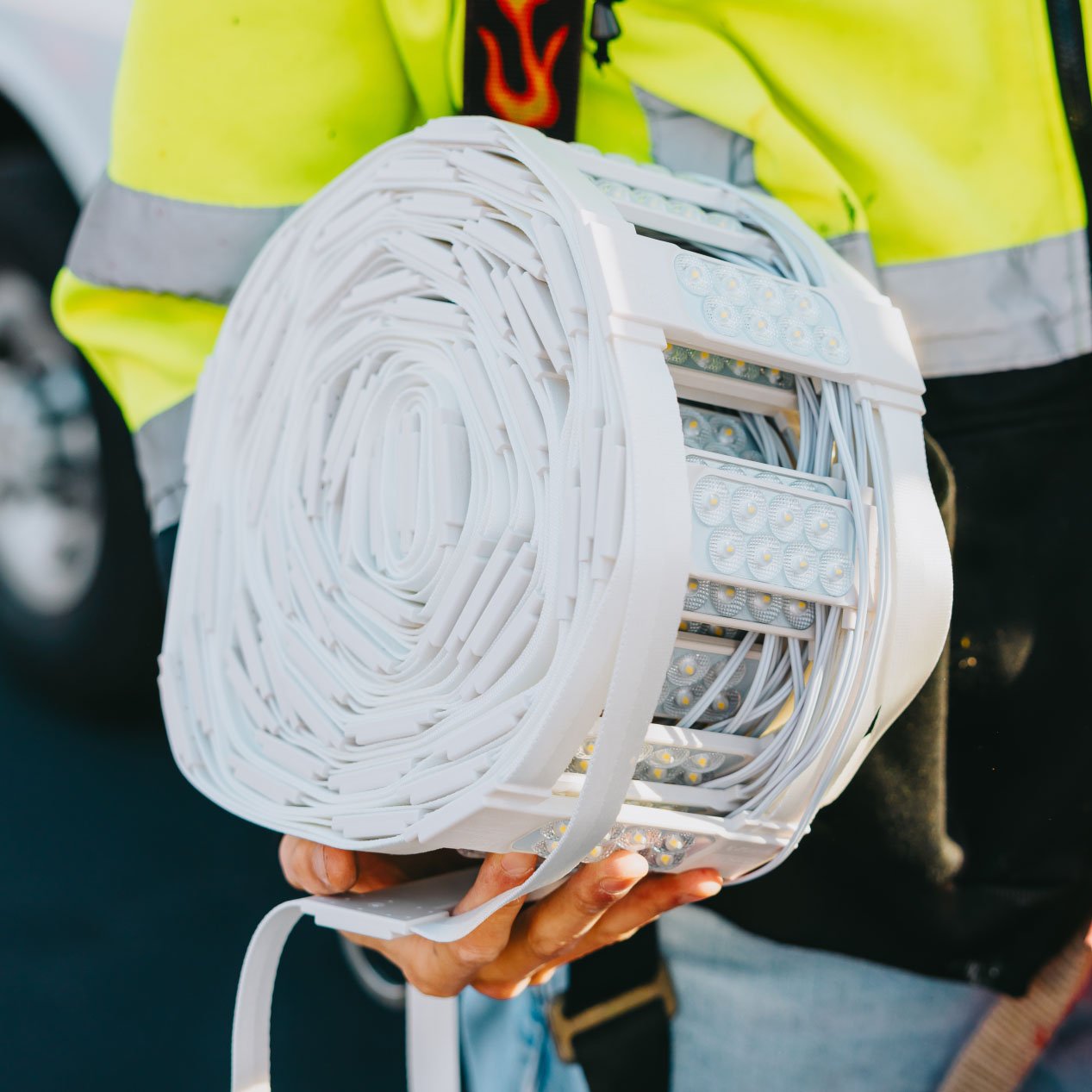 Close-up of Tymothy Mough in safety gear holding a rolled white LED module strip used for sign retrofits — Rick Signs Chicago