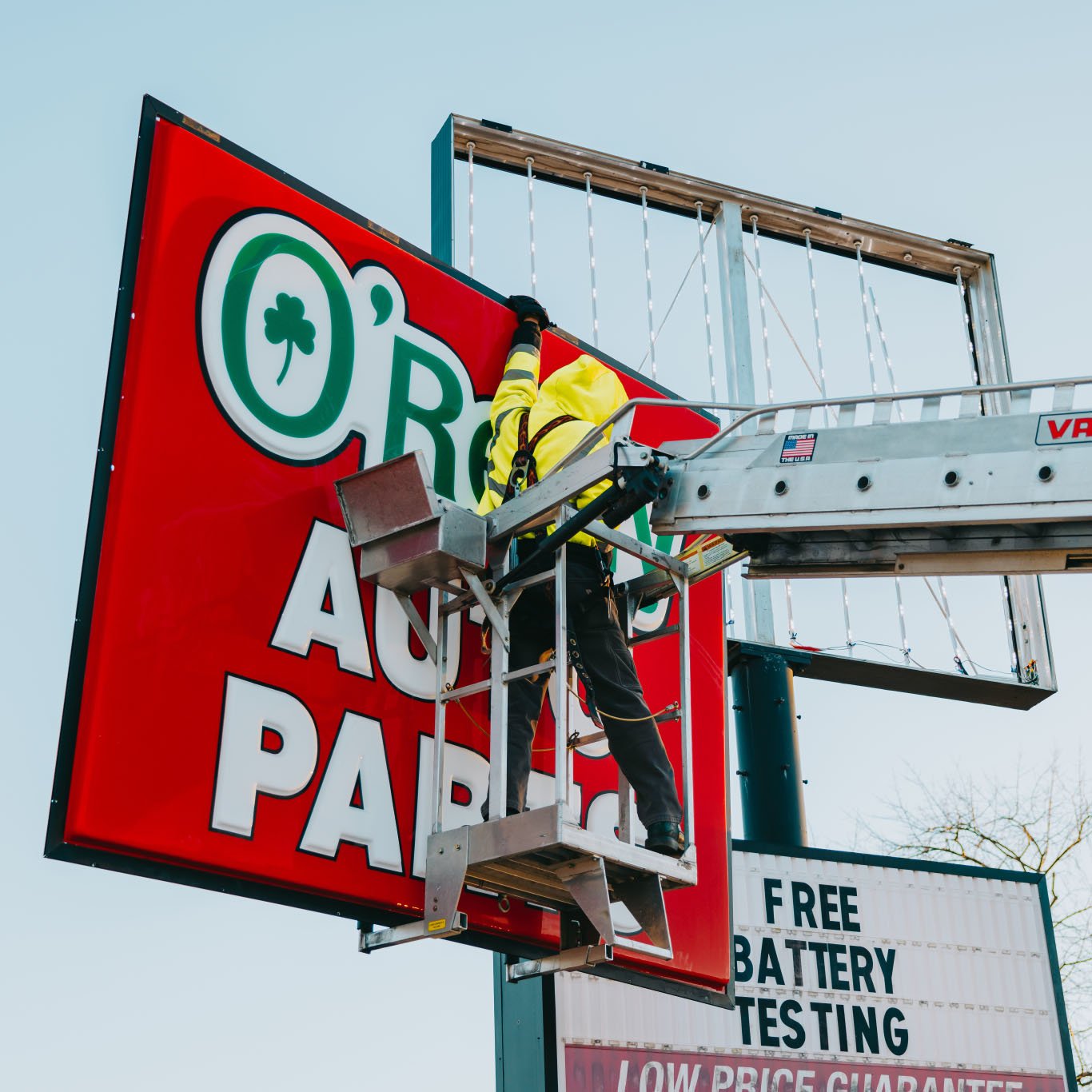 Rick Signs bucket truck servicing the O’Reilly Auto Parts pole sign with FREE BATTERY TESTING signage visible in Chicago