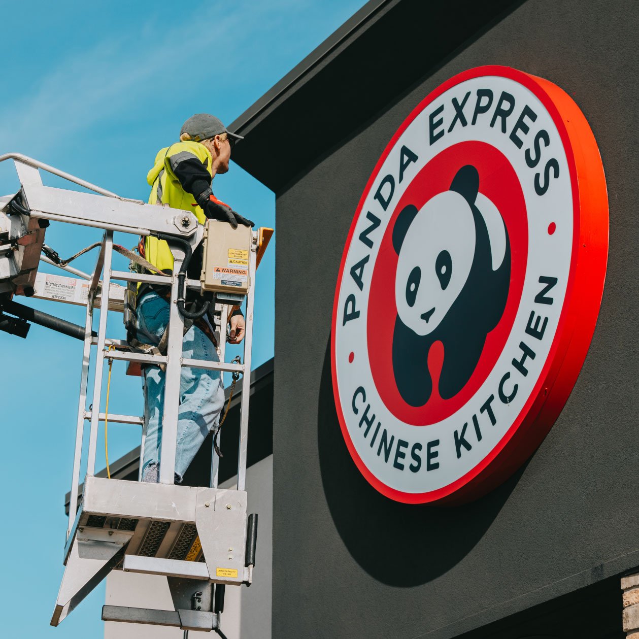 Rick Signs technician in bucket truck servicing the round Panda Express logo storefront sign in Chicago