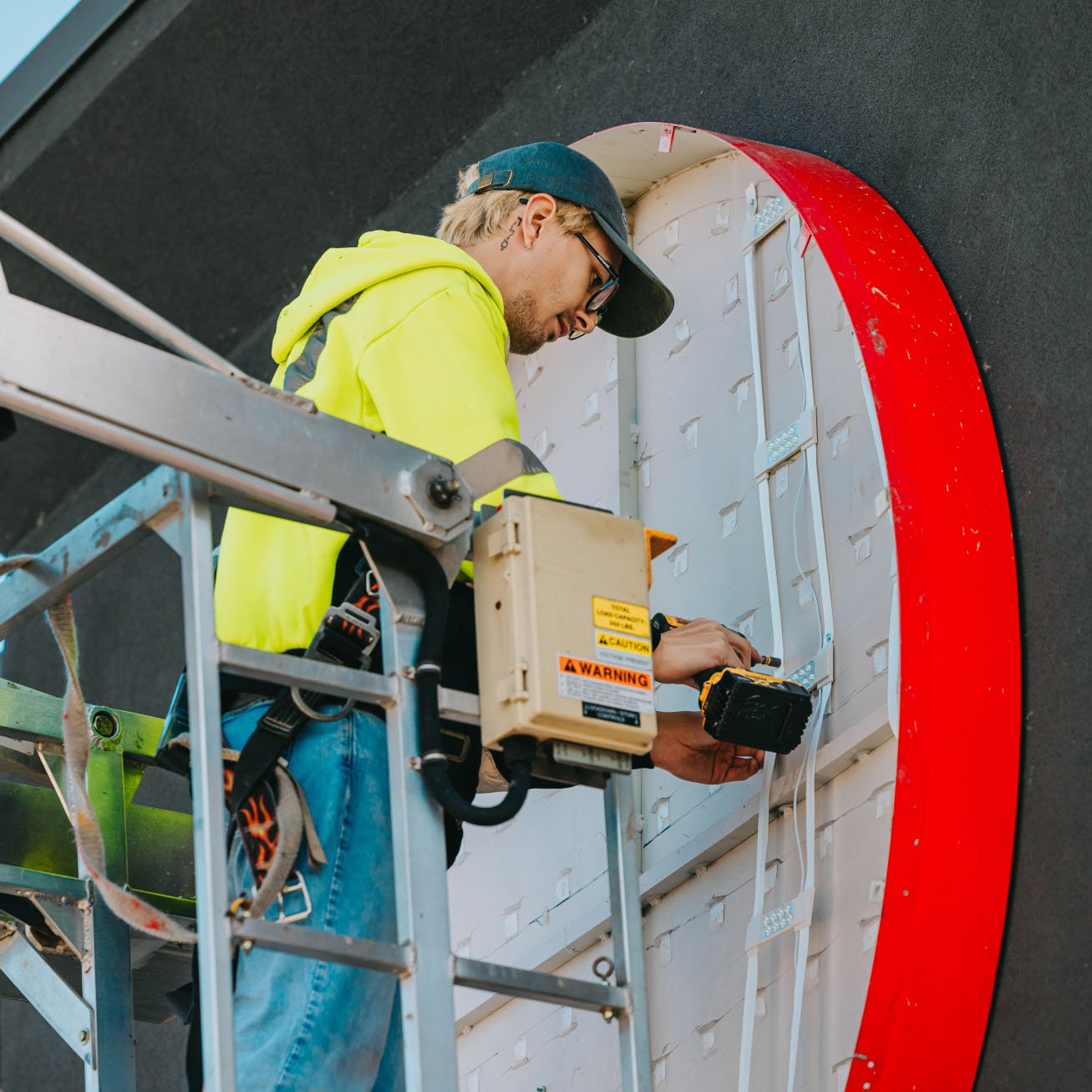 Tymothy Mough working from a bucket truck on the curved red edge of an illuminated channel letter sign — Rick Signs Chicago