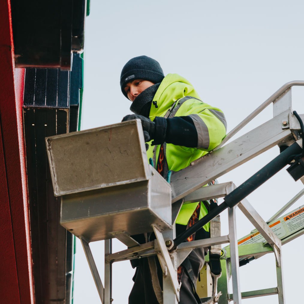 Rick Signs technician in safety harness repairing a storefront illuminated sign from the Van Ladder bucket truck in Chicago