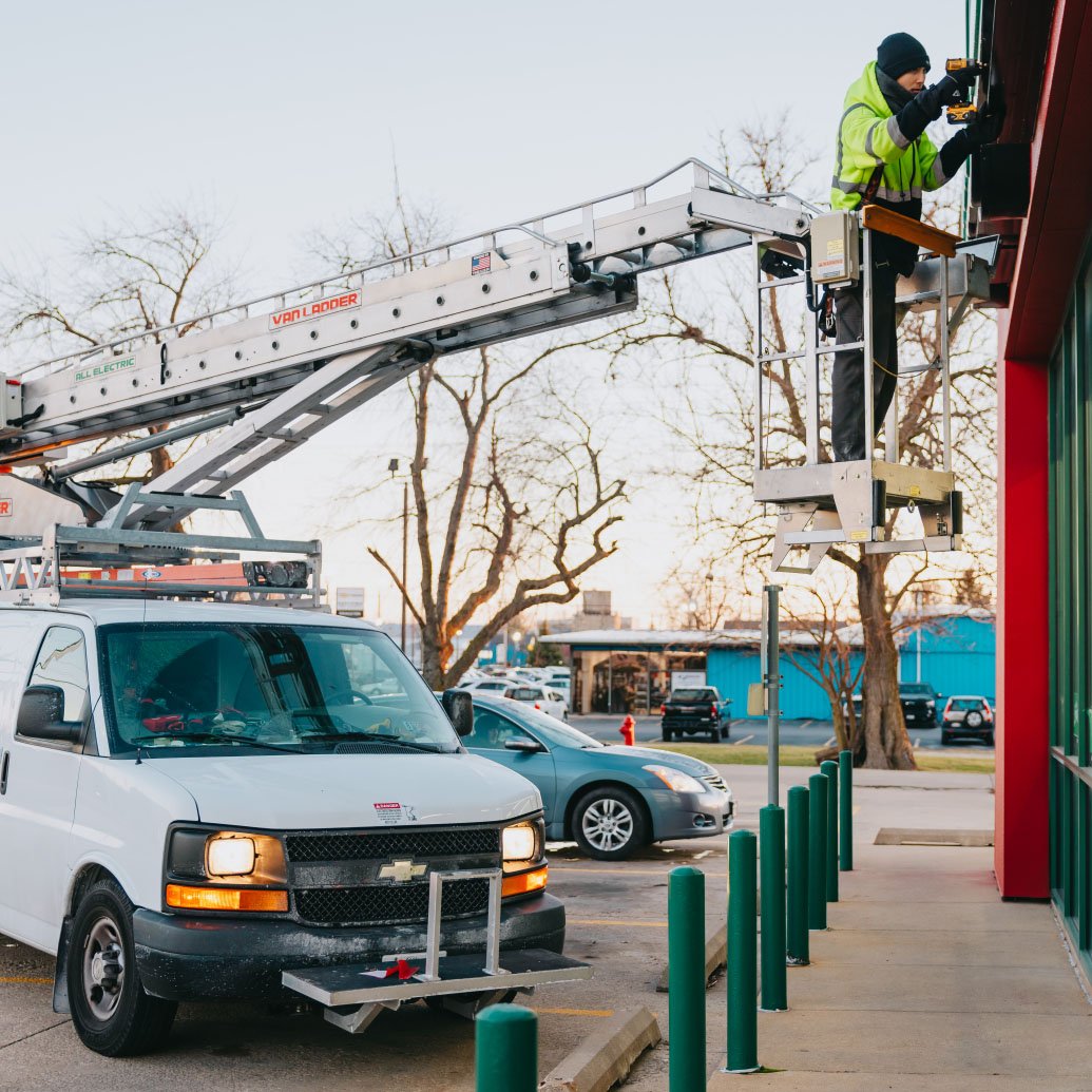 Rick Signs Van Ladder bucket truck extended high to reach an illuminated commercial sign in Chicago