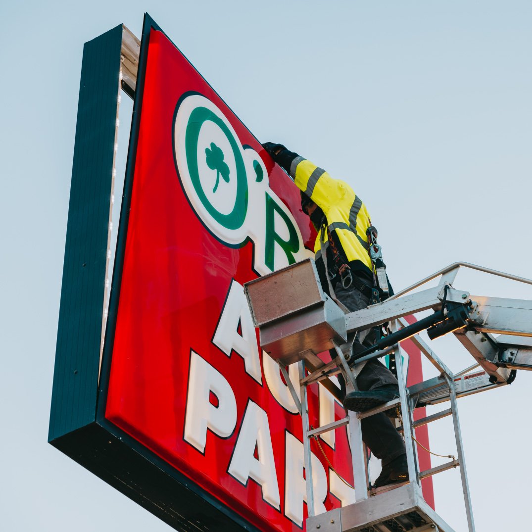 Close-up of the red O’Reilly Auto Parts cabinet sign with Rick Signs bucket truck in frame — Chicago sign repair