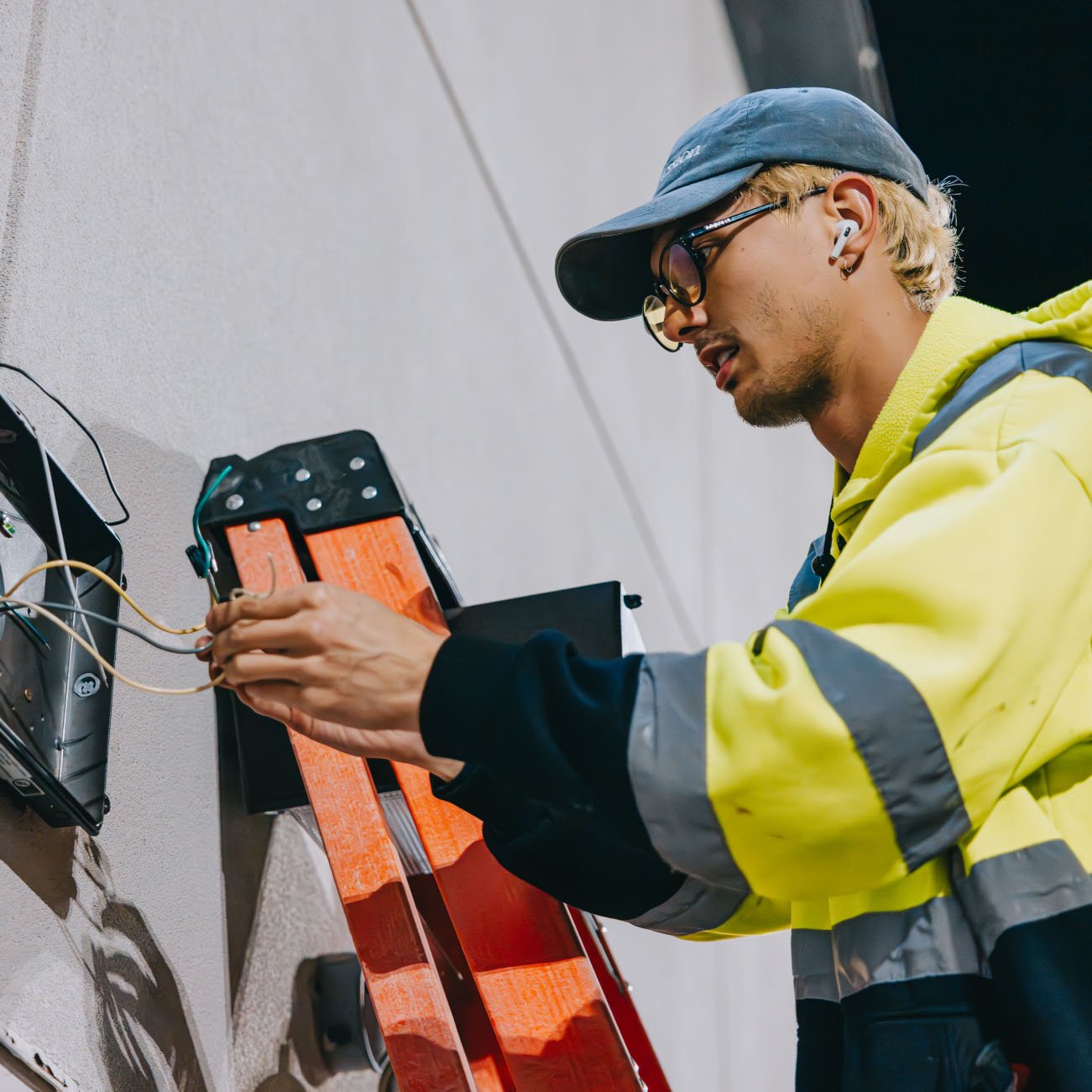 Close-up of Tymothy Mough in safety gear holding a cordless drill during a Rick Signs sign repair job in Chicago