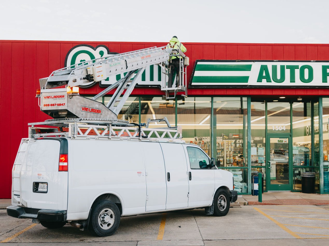 Rick Signs service van with mounted bucket truck parked at an O’Reilly Auto Parts storefront in Chicago for a sign repair job