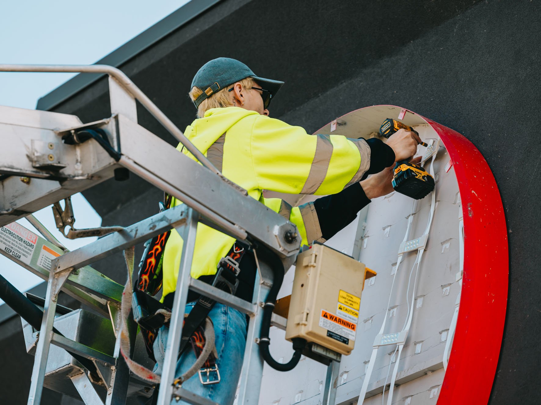 Tymothy Mough drilling and re-mounting LED modules inside a curved illuminated channel letter sign on a bucket truck — Rick Signs Chicago