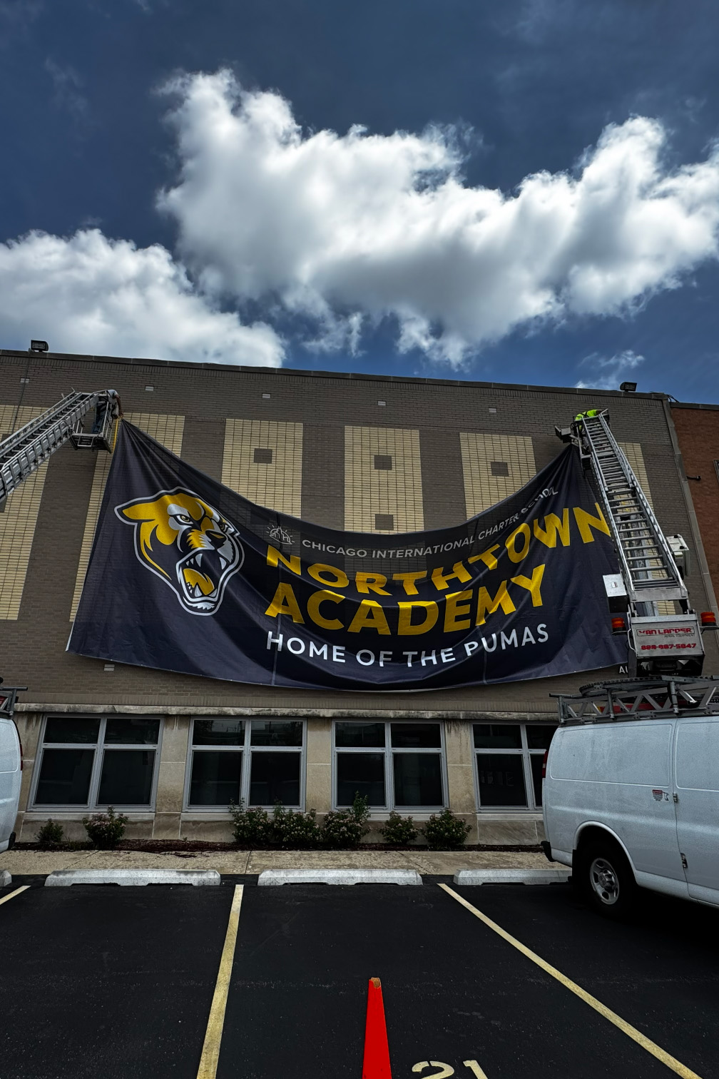 Two workers hanging a large Northtown Academy banner with a puma logo on a building's exterior wall.