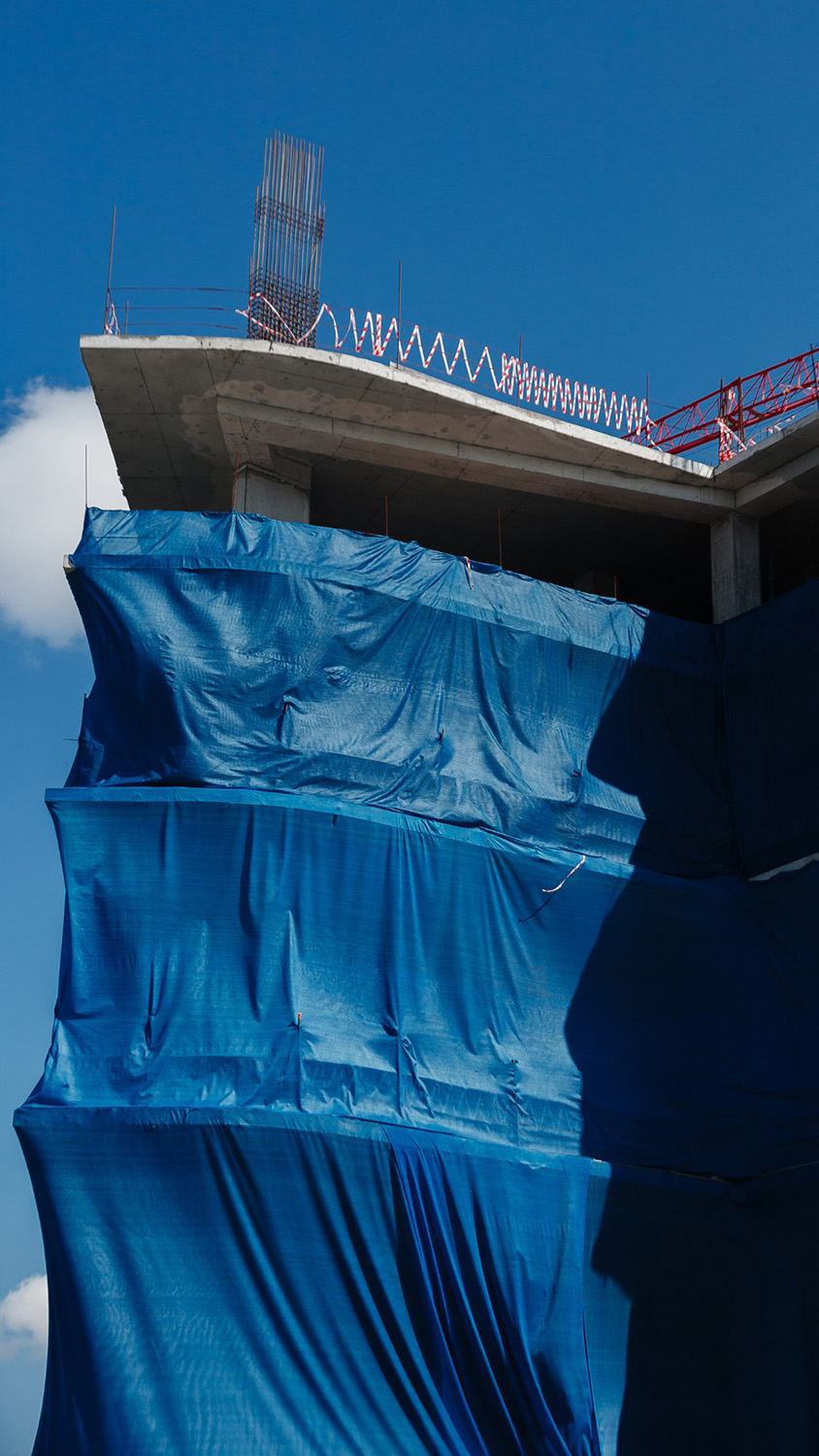 Building under construction covered with blue protective tarps against a clear blue sky.