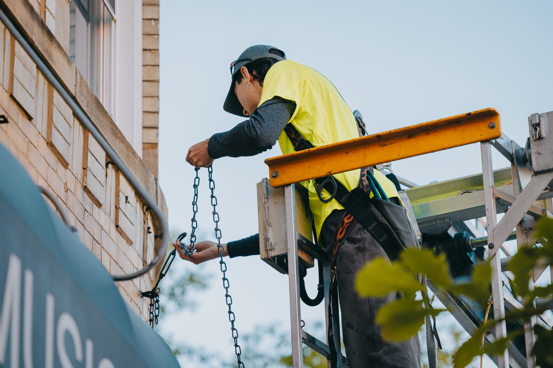 Technician attaching the chain suspension that carries a projecting sign cabinet — Rick Signs & Repairs Chicago