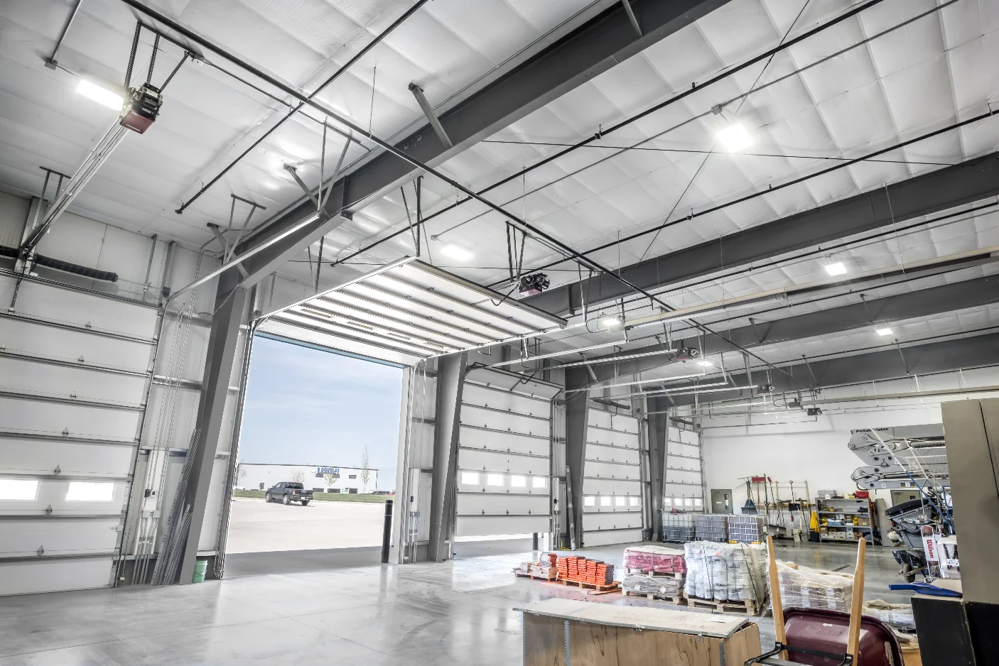 Spacious industrial garage with large overhead doors, a concrete floor, and stored equipment.