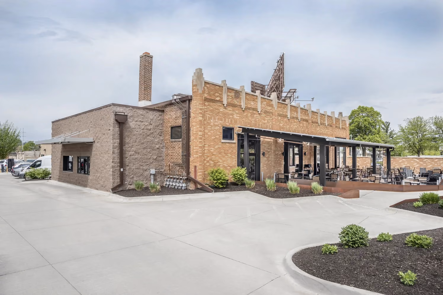 Brick building with a covered outdoor patio seating area and landscaped grounds on a cloudy day.