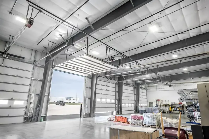 Spacious industrial garage with large overhead doors, a concrete floor, and stored equipment.