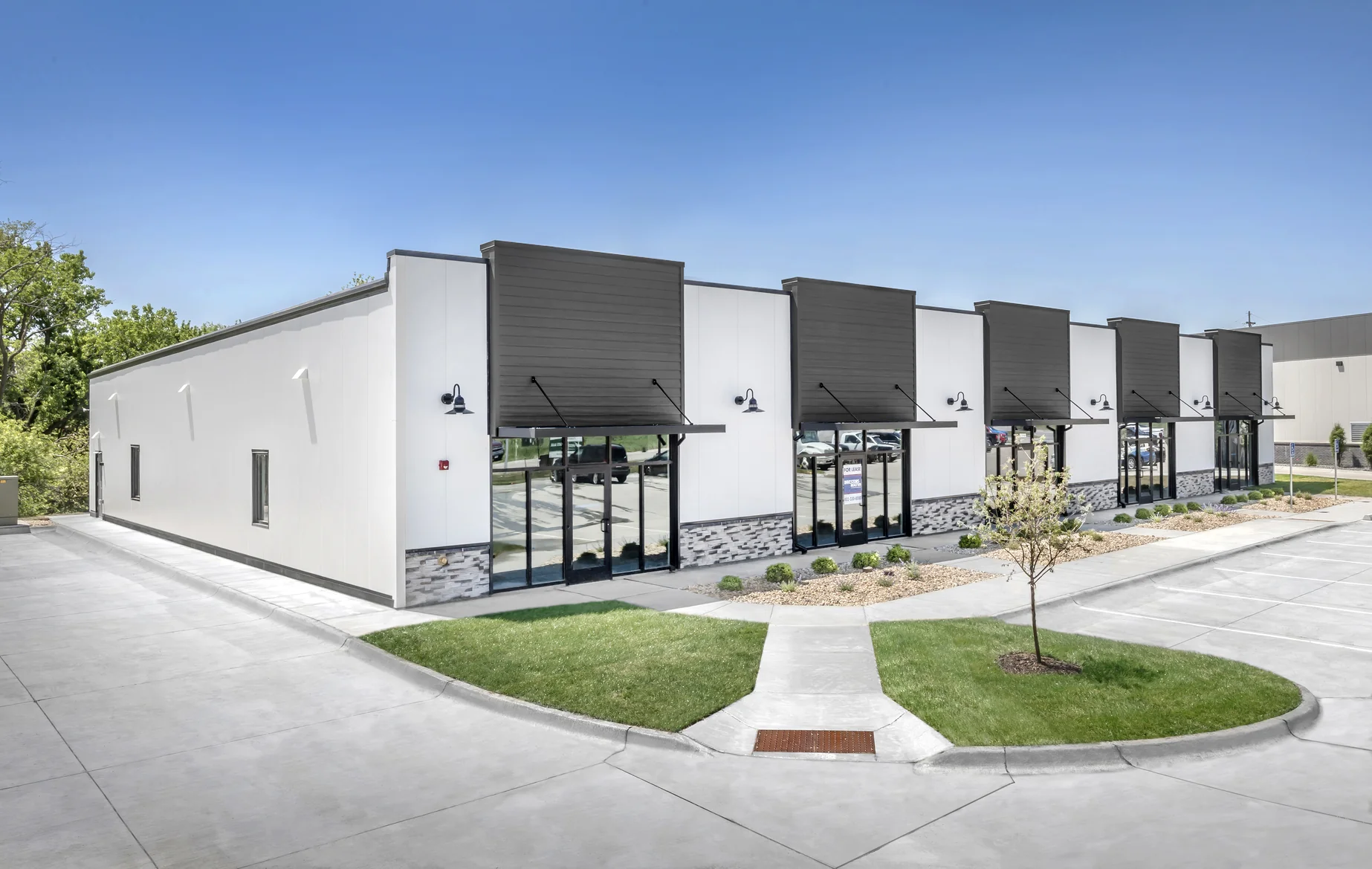 Modern commercial building with multiple glass-door entrances and small landscaped areas in front.