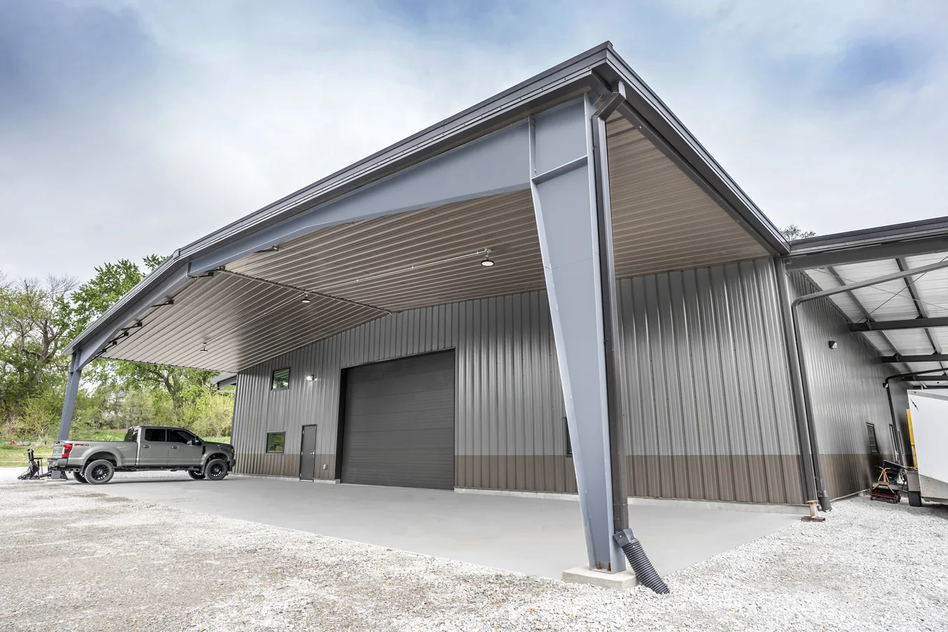 Gray steel building with cantilever canopy and black truck parked on gravel outside.