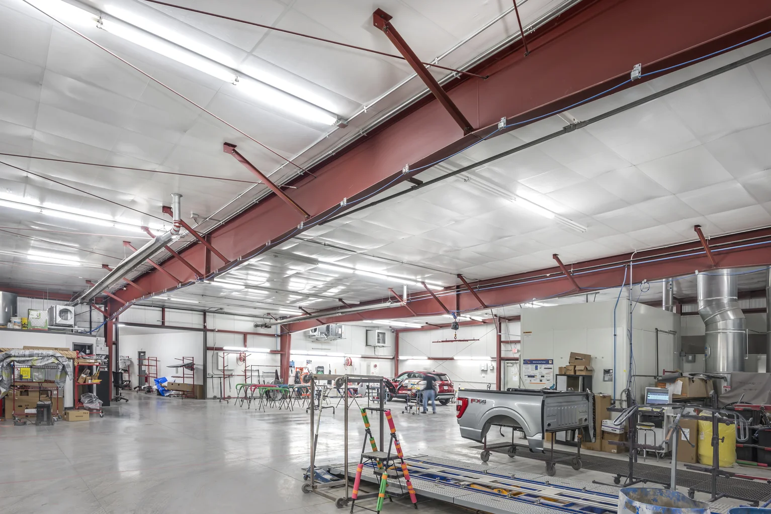 Spacious auto body shop interior with car parts, workstations, and a vehicle being repaired.