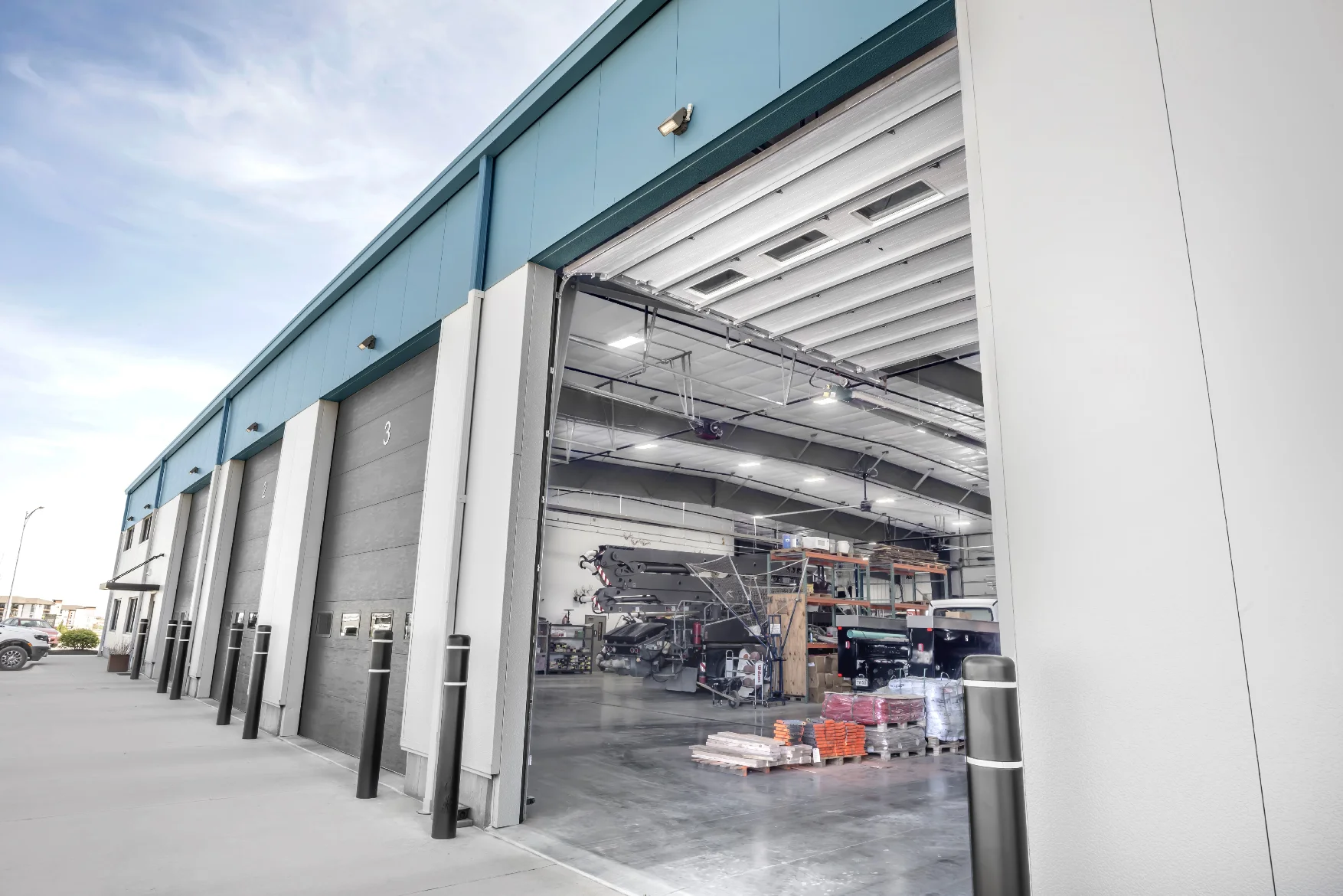 Industrial garage with multiple bay doors, one open showing pallets and equipment inside.