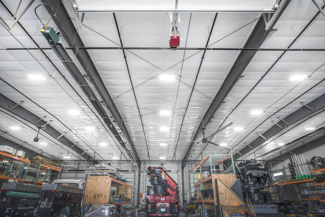 Interior of a large industrial warehouse with shelves, equipment, and a red crane truck in the center.