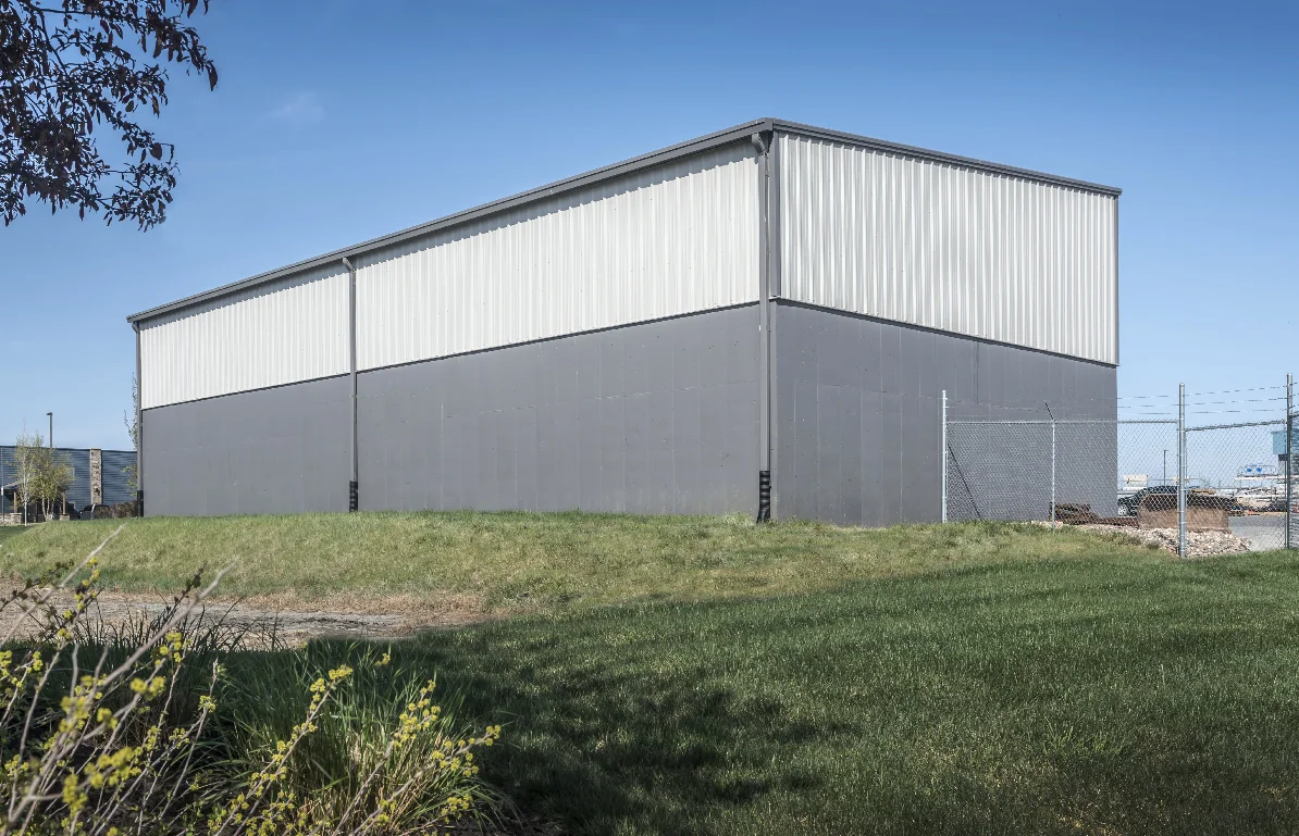 Gray and white industrial storage building with a grassy foreground under a clear blue sky.