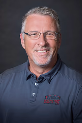 Headshot of an older Midwest Erectors crew member with glasses and gray hair, wearing a gray company polo