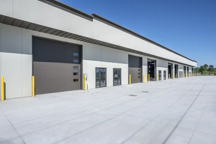 Exterior of a modern industrial warehouse with multiple large loading bay doors and concrete pavement.