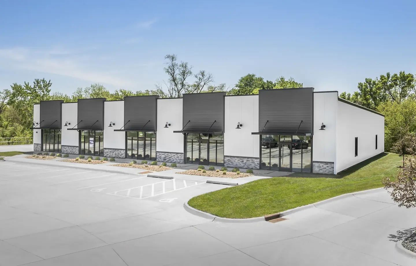 New commercial warehouse building with multiple glass entrances and parking spaces outside.
