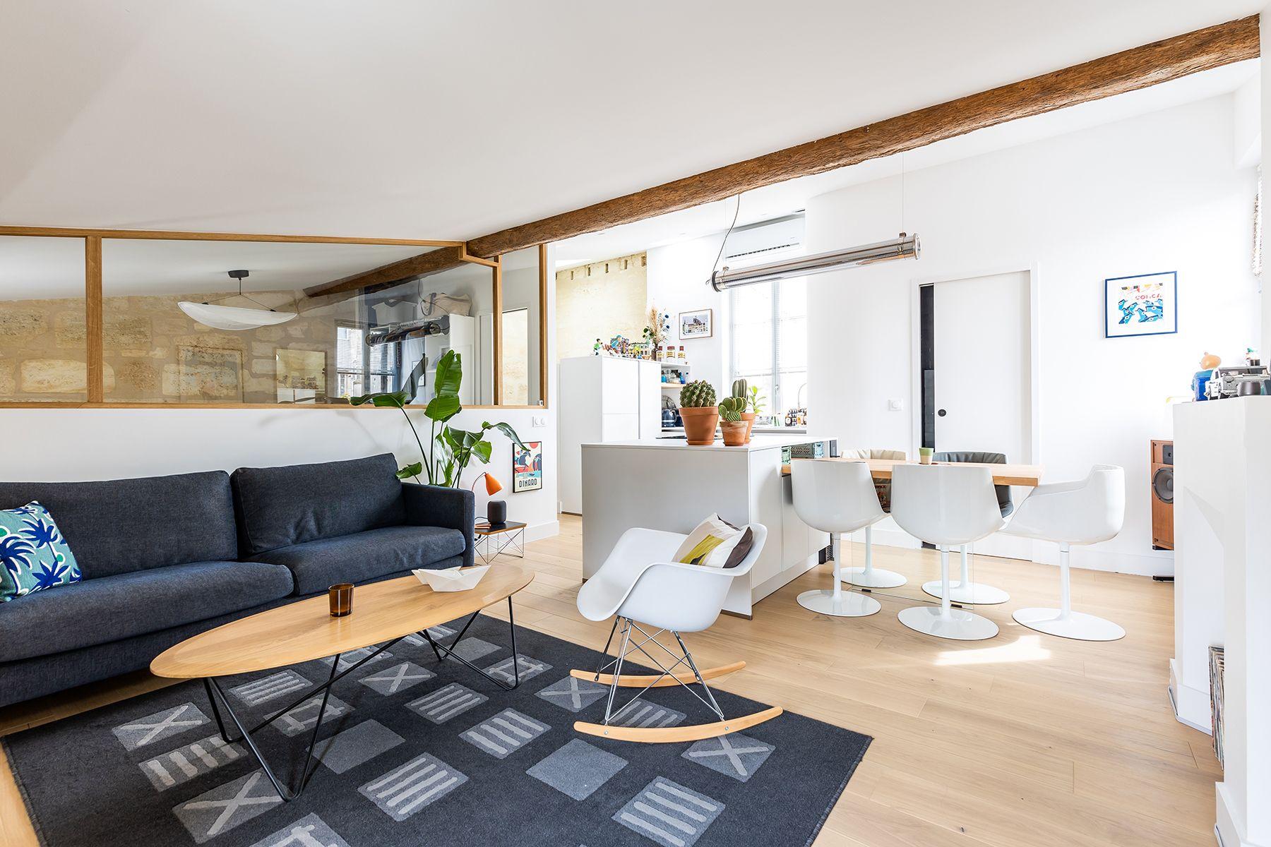 Modern white kitchen with large marble island, black hardware, pendant lights, stainless appliances, and wood floors.