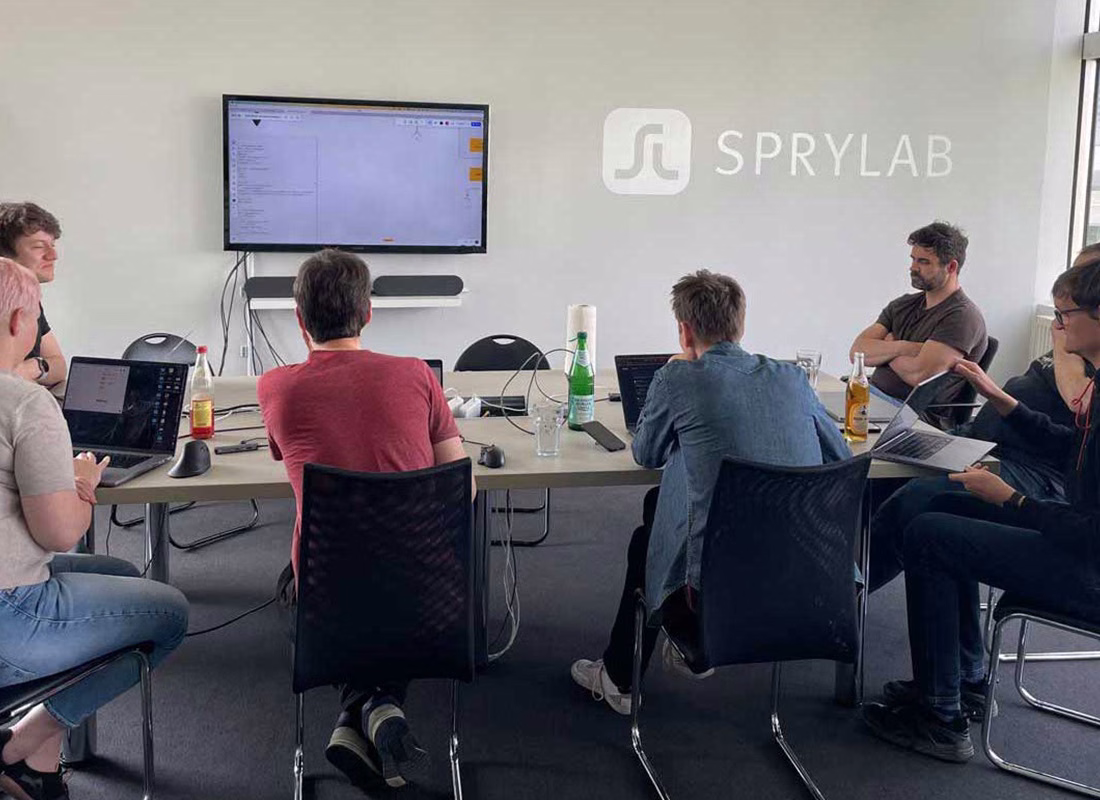 SPRYLAB-Team arbeitet beim Hackathon mit Laptops an einem Konferenztisch vor einem großen Bildschirm