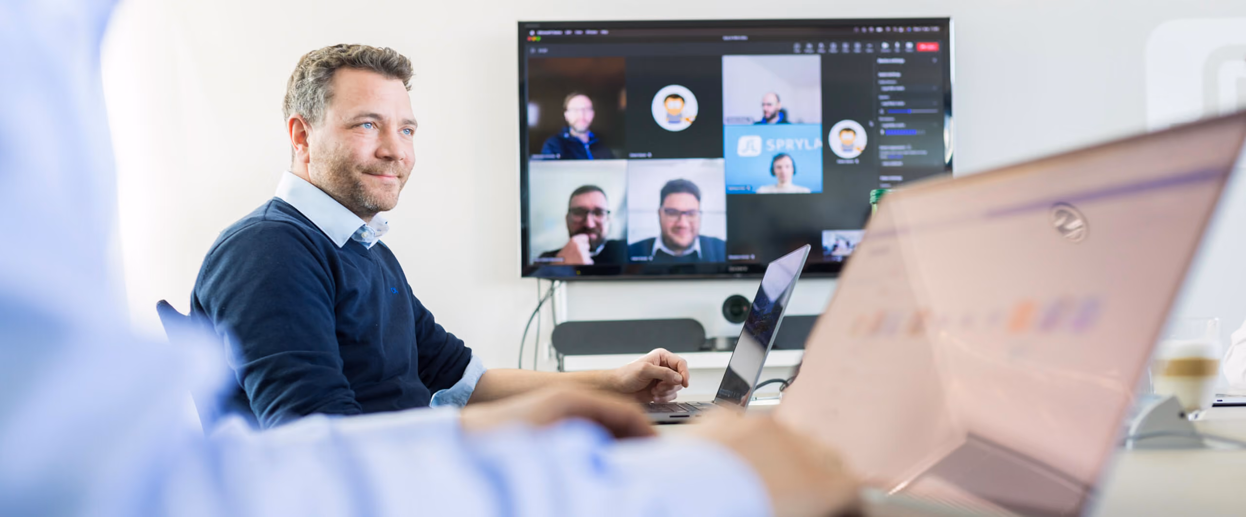 Mann bei Online-Meeting am Laptop, Bildschirm zeigt mehrere Teilnehmer in Videokonferenz.