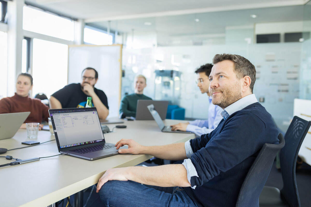 Menschen in einem Meeting sitzen um einen Tisch mit Laptops in einem modernen Büro.