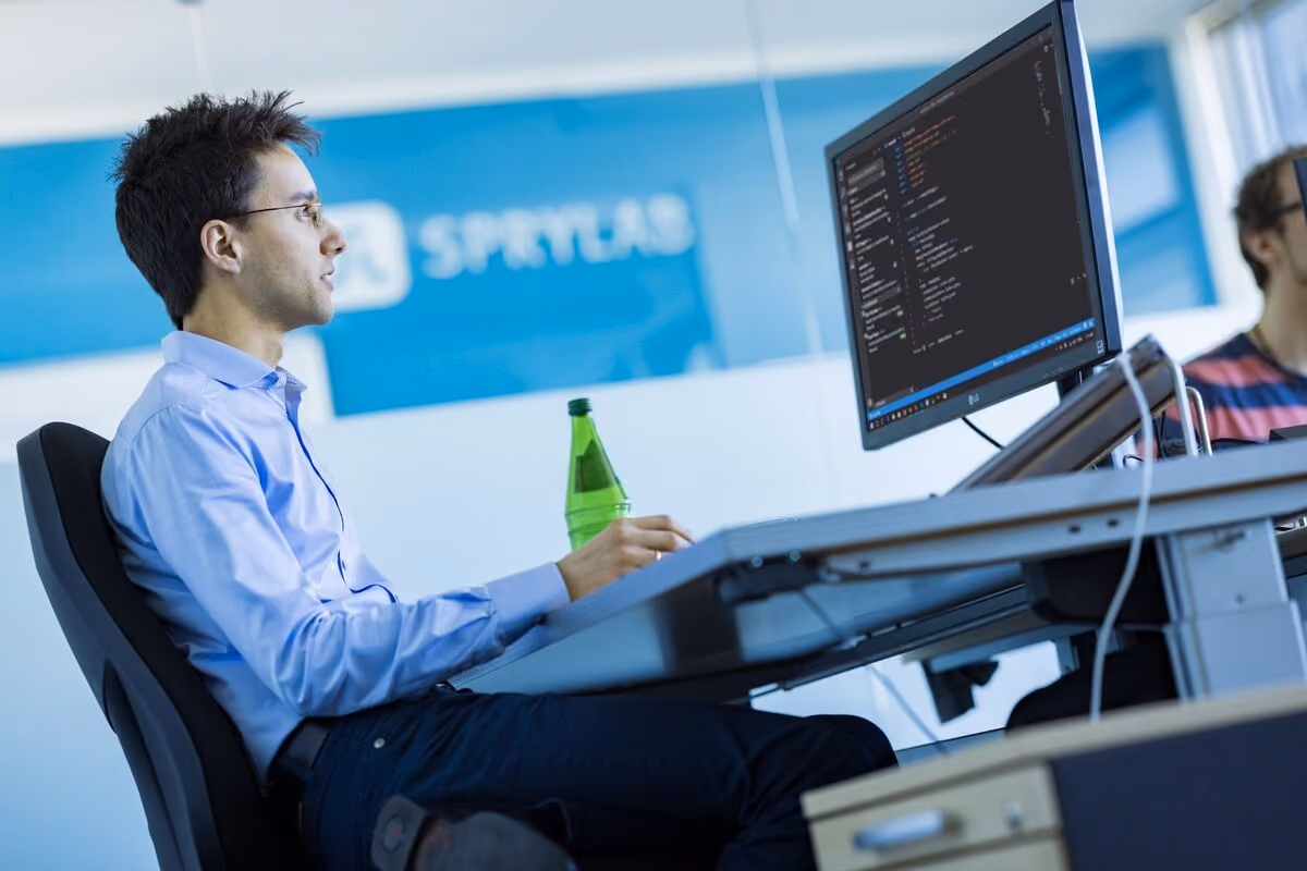 Mann in Hemd arbeitet an Computer mit Programmiercode in einem modernen Büro.