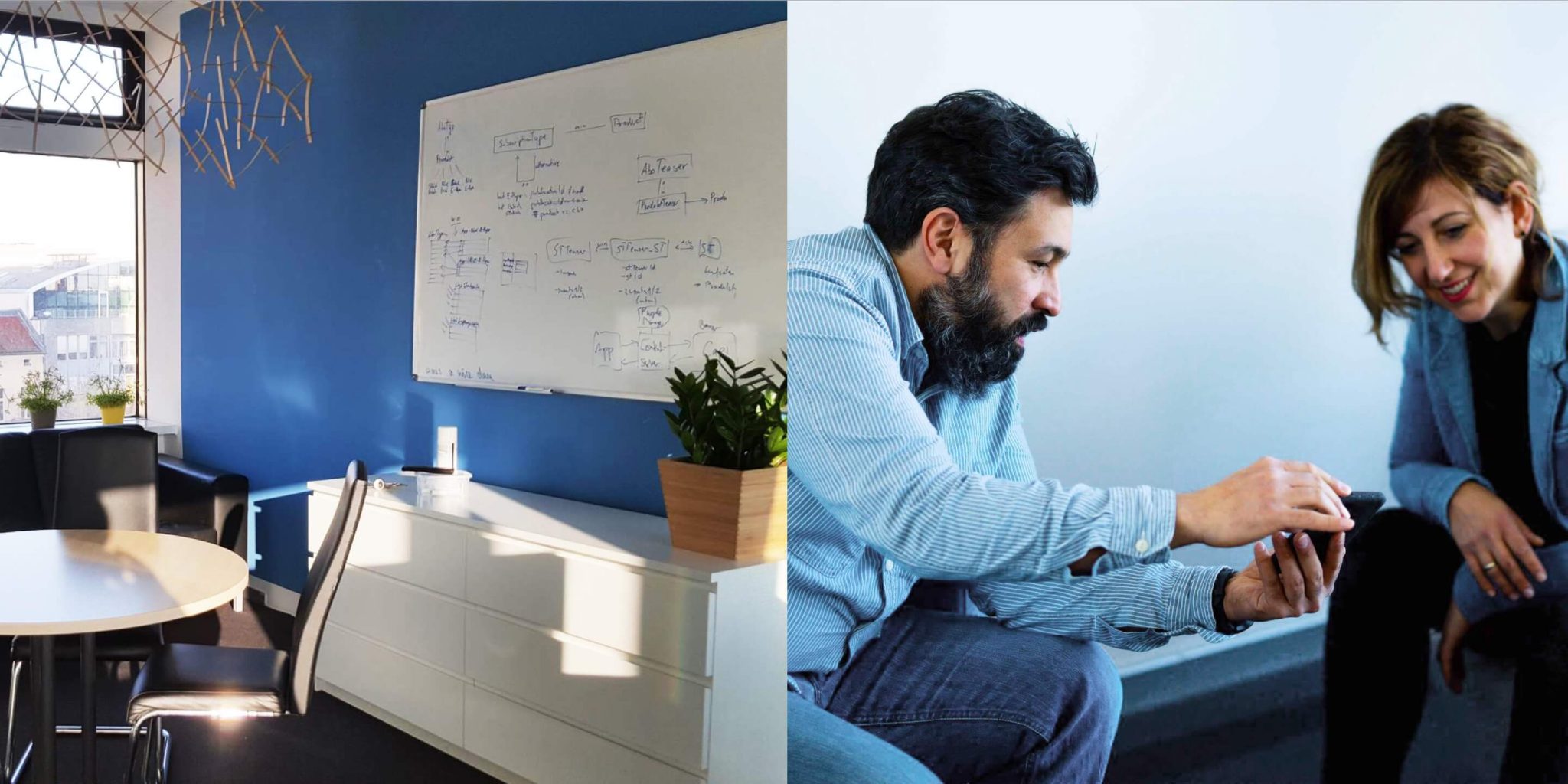 Besprechungsraum mit Whiteboard neben zwei Personen, die gemeinsam auf ein Smartphone schauen.