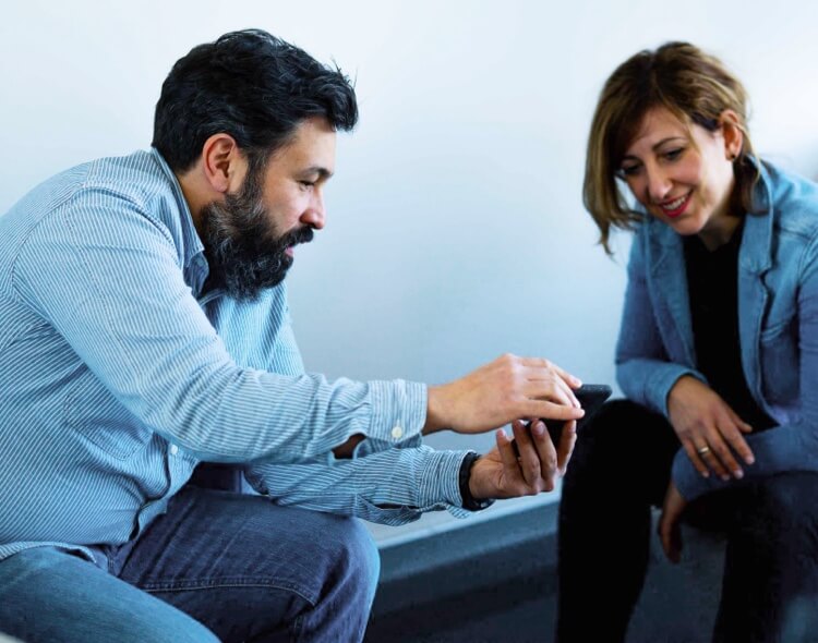 Ein Mann zeigt einer Frau auf einem Smartphone etwas, beide sitzen und lächeln.
