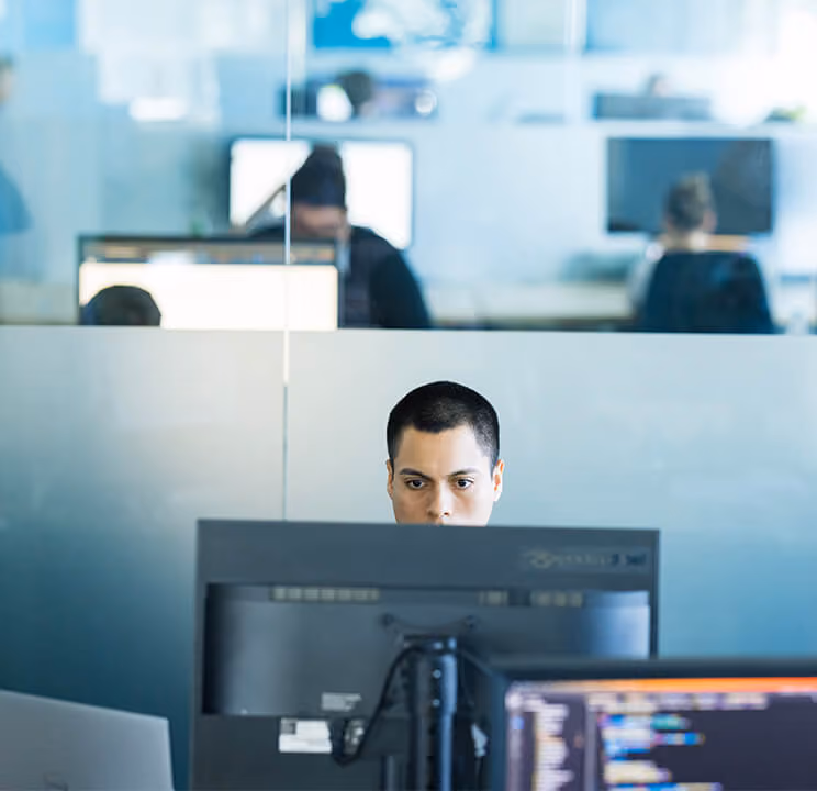 Person arbeitet konzentriert vor zwei Computermonitoren in einem modernen Büro.