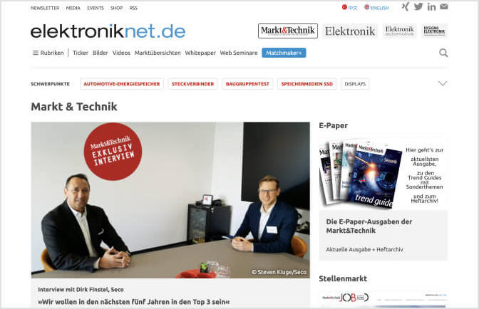 Zwei Männer in Anzügen sitzen an einem Tisch in einem Interview bei elektroniknet.de.