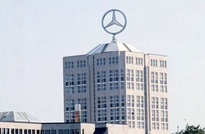 Hochhaus mit großem Mercedes-Stern auf dem Dach unter hellem Himmel.
