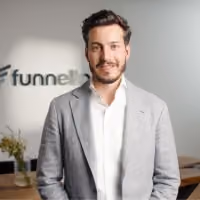 Junger Mann mit grauem Sakko steht vor einem verschwommenen Funnell-Logo in einem Büro.