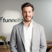 Junger Mann mit grauem Sakko steht vor einem verschwommenen Funnell-Logo in einem Büro.
