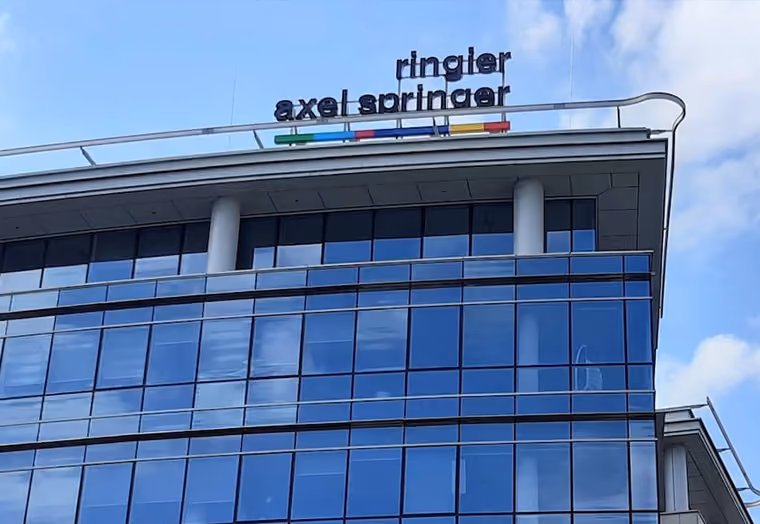 Moderne Glasfassade eines Bürogebäudes mit Schriftzug ringier axel springer oben am Dach.